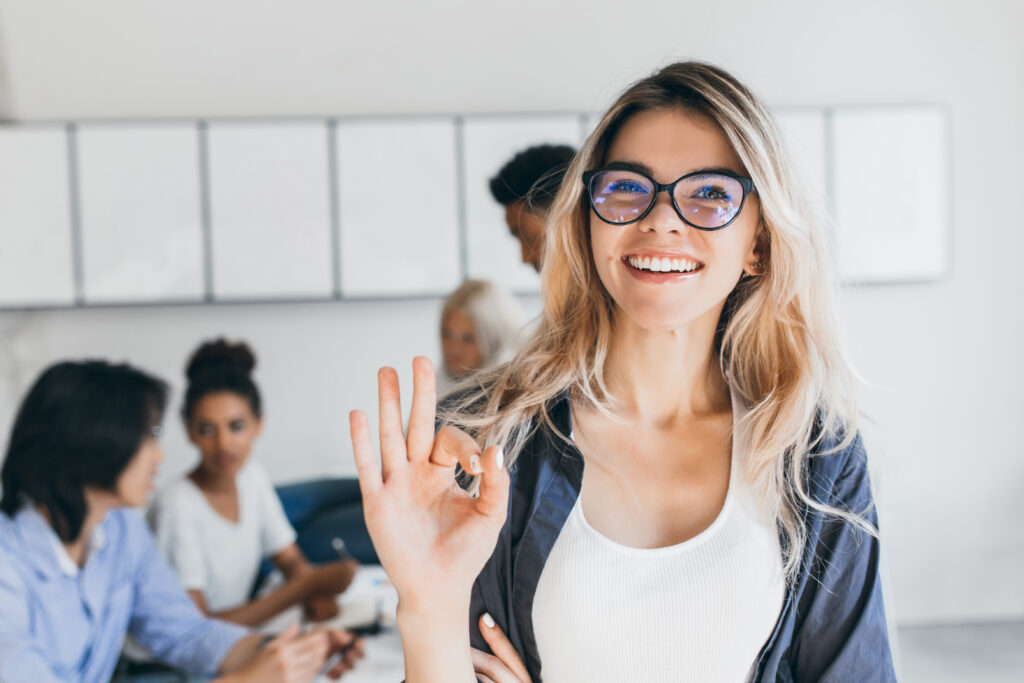 Necesitas Comunicar? Bienvenid@! Close Up Portrait Of Pretty Female Manager From Sales Department Indoor Photo Of Smiling Woman Working In Office With Discussing People 1024x683